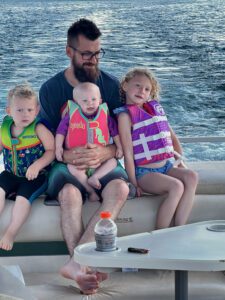Dad and his three kids sitting on a boat in Higgins lake. One of the best Michigan Camping Spots. 